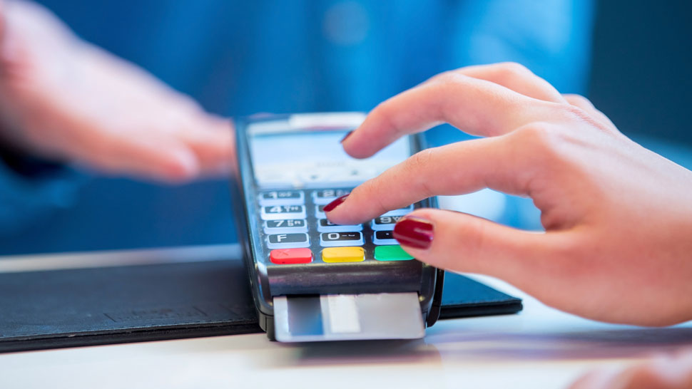 Roka z rdeče nalakiranimi nohti pritiska številko na POS terminalu med vnosom PIN kode za plačilo s kartico.