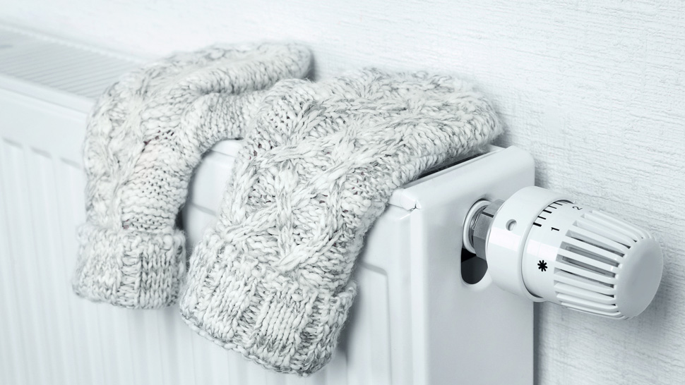 Na sliki je bela radiatorjska grelna naprava, na kateri sušijo volnene rokavice svetle barve. Na desni strani radiatorja je razviden tudi termostatski regulator temperature.