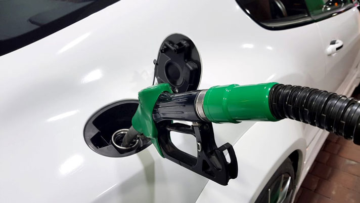 Na sliki je bel avtomobil, ki se polni z gorivom. V rezervoar je vstavljena črpalka z zelenim ročajem, kar običajno označuje točenje dizelskega goriva.