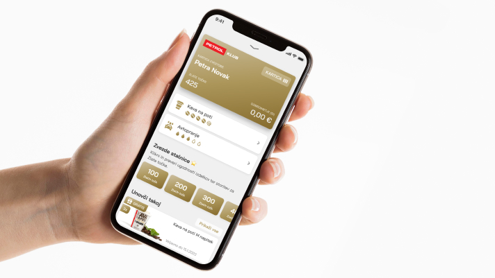 Na sliki je roka, ki drži pametni telefon z odprto aplikacijo. Na zaslonu so vidni podatki uporabnika prikaz zbranih zlatih točk, možnost koriščenja nagrad in pregled ugodnosti.