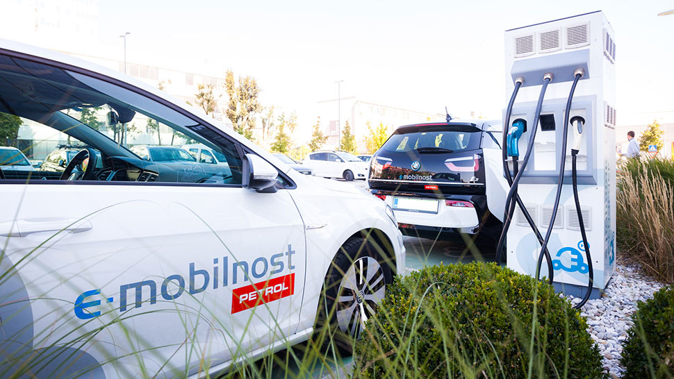 Slika prikazuje električna vozila pri polnilni postaji Petrol e-mobilnost s kabli za hitro polnjenje.
