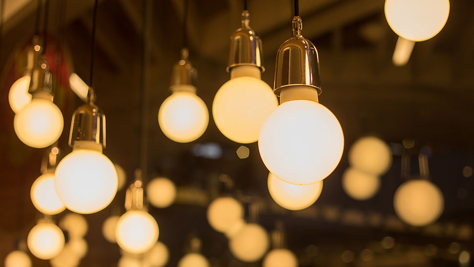 Na sliki je več visečih žarnic z okroglimi svetilkami, ki oddajajo toplo rumeno svetlobo.