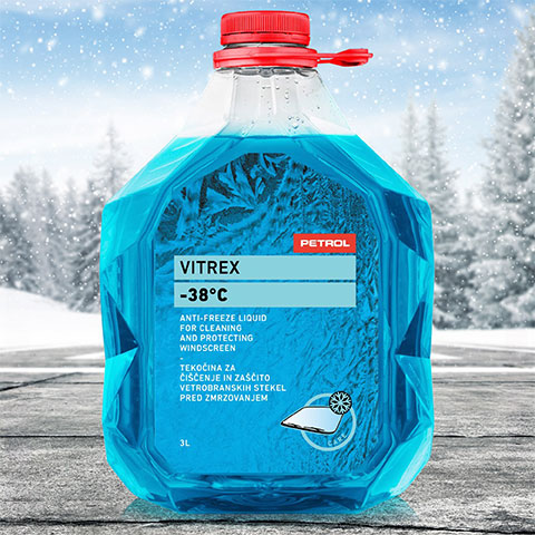 Plastenka modrega čistila Vitrex -38°C za vetrobranska stekla s Petrolovo oznako in rdečim pokrovčkom, postavljena na cesti s sneženo pokrajino v ozadju.