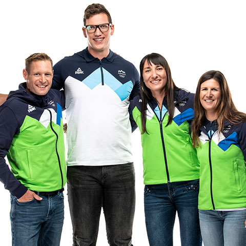 Štirje nasmejani športniki v zeleno-modrih reprezentančnih jopičih stojijo skupaj in se prijateljsko objemajo.