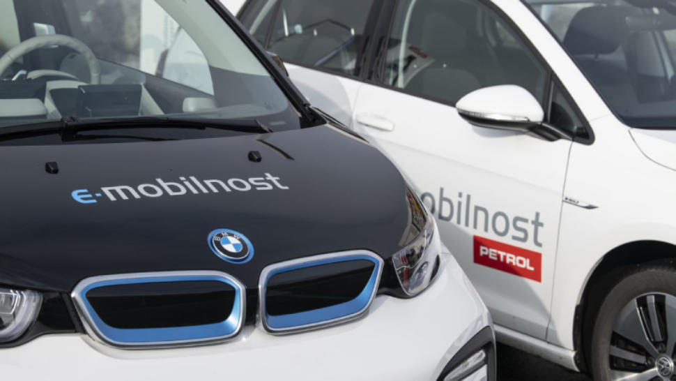 Na sliki sta dva avtomobila z oznako »e-mobilnost Petrol«. Vozili sta parkirani eno ob drugem, v ospredju je črno-bela znamke BMW, v ozadju pa belo vozilo z enako oznako.