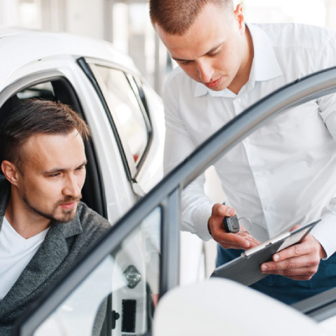 Nas liki moški sedi v avtomobilu in se pogovarja z drugim moškim, ki stoji ob vozilu in drži tablico ter avtomobilske ključe. Prizor prikazuje svetovanje ali pregled vozila v okviru upravljanja in vzdrževanja voznega parka v svetlem, sodobnem prostoru.