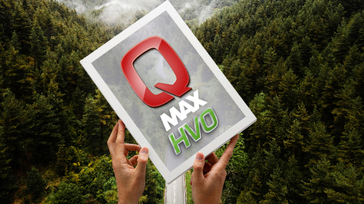 Na sliki oseba drži letak z logotipom Q Max HVO pred gostim zelenim gozdom.