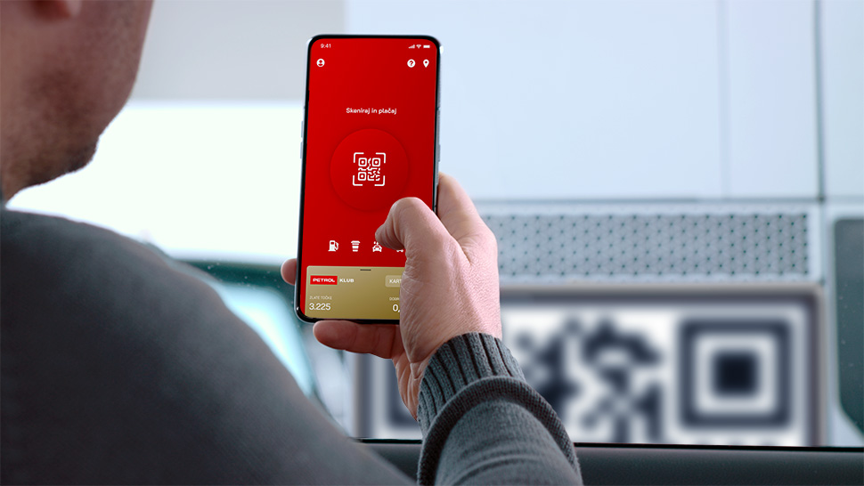 Moški v avtomobilu ima na telefonu odprto Petrol aplikacijo z QR kodo in skenira drugo QR kodo, ki je prikazana v ozadju."