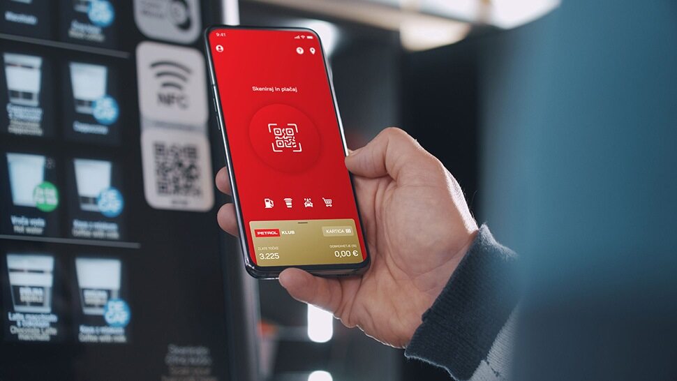 Oseba drži pametni telefon z odprto Petrol aplikacijo, pripravljeno na skeniranje QR kode pri kavomatu.