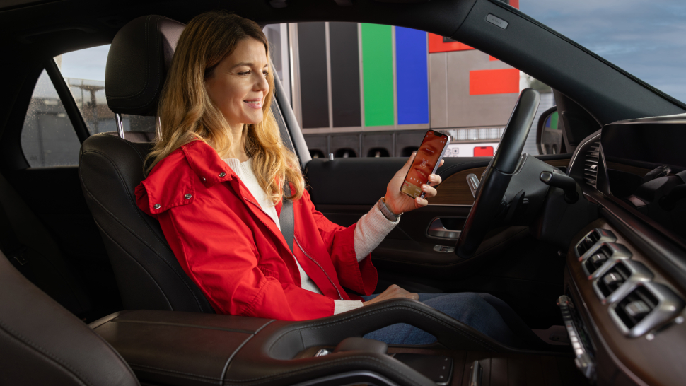 Ženska v rdeči jakni sedi v avtomobilu in uporablja Petrolovo mobilno aplikacijo na pametnem telefonu.