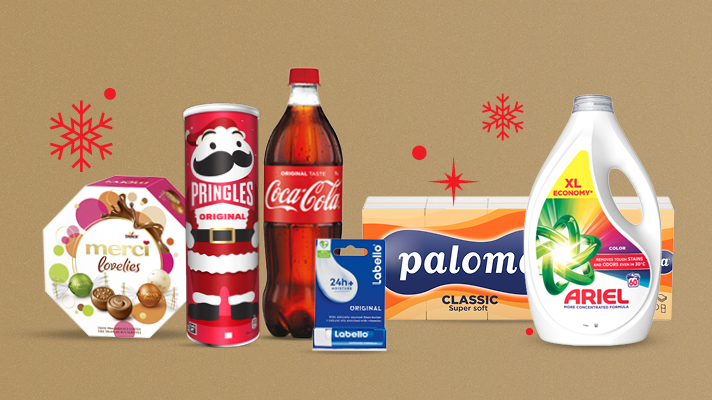 Izdelki na svetlo rjavo-zlatem ozadju:Bonboniera Merci Lovelis 185 g, čips Pringles Original v praznični embalaži, plastenka Coca-Cola 1 L, balzam za ustnice Labello Original, papirnate brisače Paloma Classic super soft in pralni gel Ariel Color XL Economy. V ozadju so dodane rdeče snežinke.