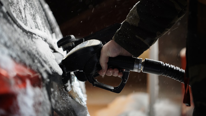 Na sliki oseba drži gorivo točilno ročko in toči gorivo v avtomobil. Avto je prekrit z vodo in peno.