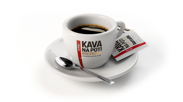 Bela skodelica Espresso kave na belem krožniku z žličko in dvema paketkoma sladkorja. Na skodelici je napis 