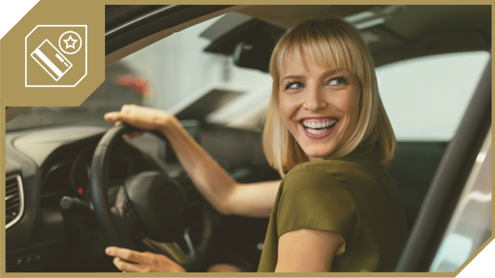 Nasmejana dekle sedi v avtomobilu na voznikovem sedežu in se veselo ozira nazaj, v levem zgornjem kotu slike je ikona kartice z zvezdico.
