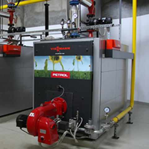 Slika prikazuje industrijski kotel znamke Viessmann s Petrolovo oznako, nameščen v tehničnem prostoru z napeljavami.