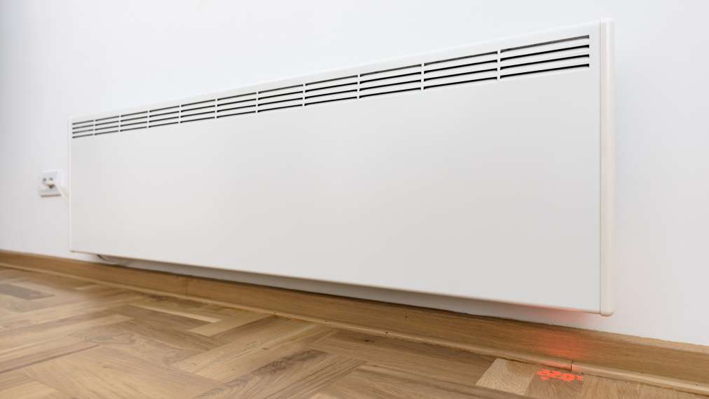 Beli električni stenski radiator nameščen v prostoru nad lesenim parketom.