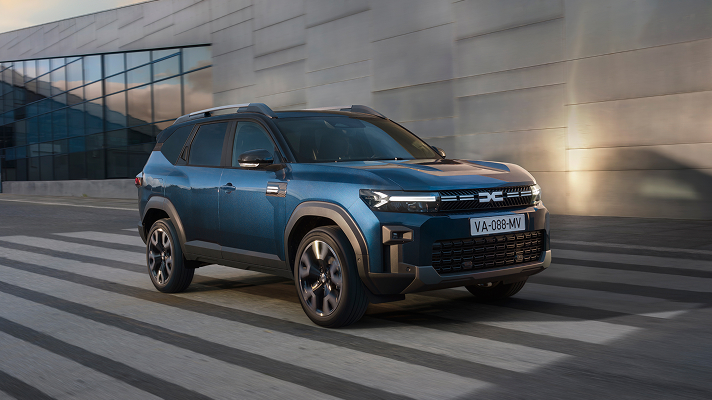 Na sliki je prikazan moder SUV vozi čez prehod za pešce pred moderno stavbo.