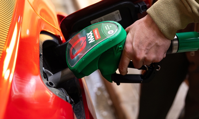 Bližnji posnetek točenja goriva v oranžen avtomobil. Roka drži zeleno točilno ročko Petrol Q Max, vstavljeno v odprtino za gorivo.