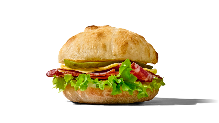 Svež sendvič Rustic, pripravljen v hrustljavi rustikalni pogačici. V njem so vidne rezine želodčeve salame, sveža zelena solata, sir, kisle kumarice ter plast kremaste majoneze.