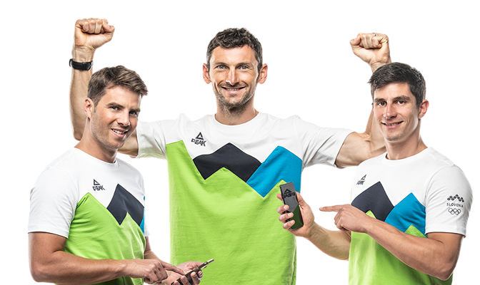 Trije slovenski športniki v olimpijskih majicah se smejijo, dvigujejo roke in držijo telefon.
