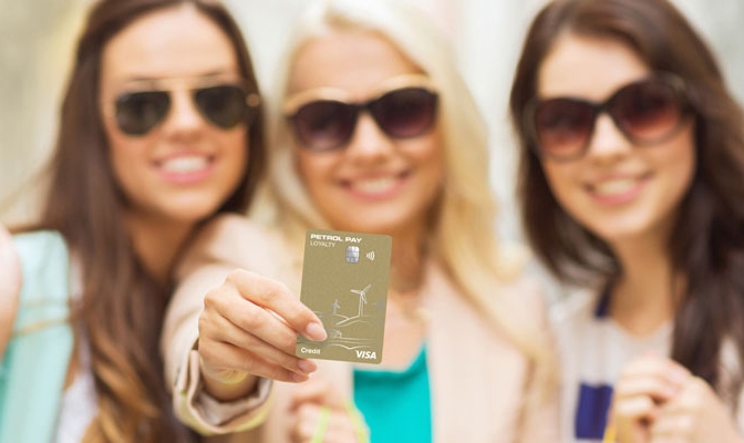 Tri nasmejana dekleta s sončnimi očali, ena v ospredju drži kartico Petrol Pay Loyalty Visa.