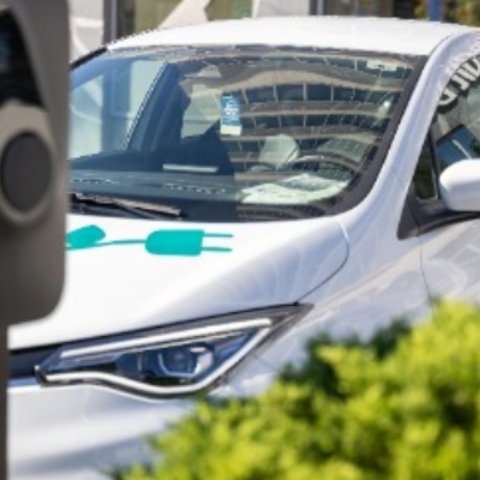 Električni avtomobil BMW i3 z grafiko e-mobilnosti in logotipom Petrol je parkiran na modro označenem parkirnem mestu pred objektom.